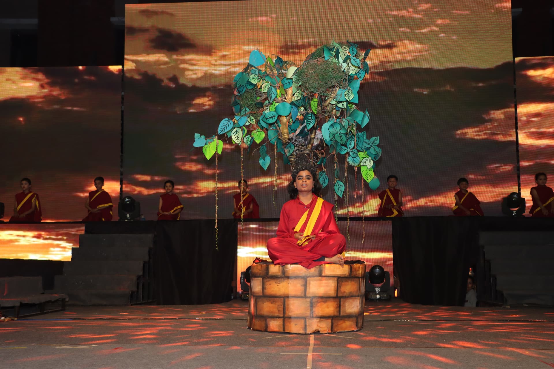 Student performing a solo act under a handcrafted tree set with LED sunset backdrop