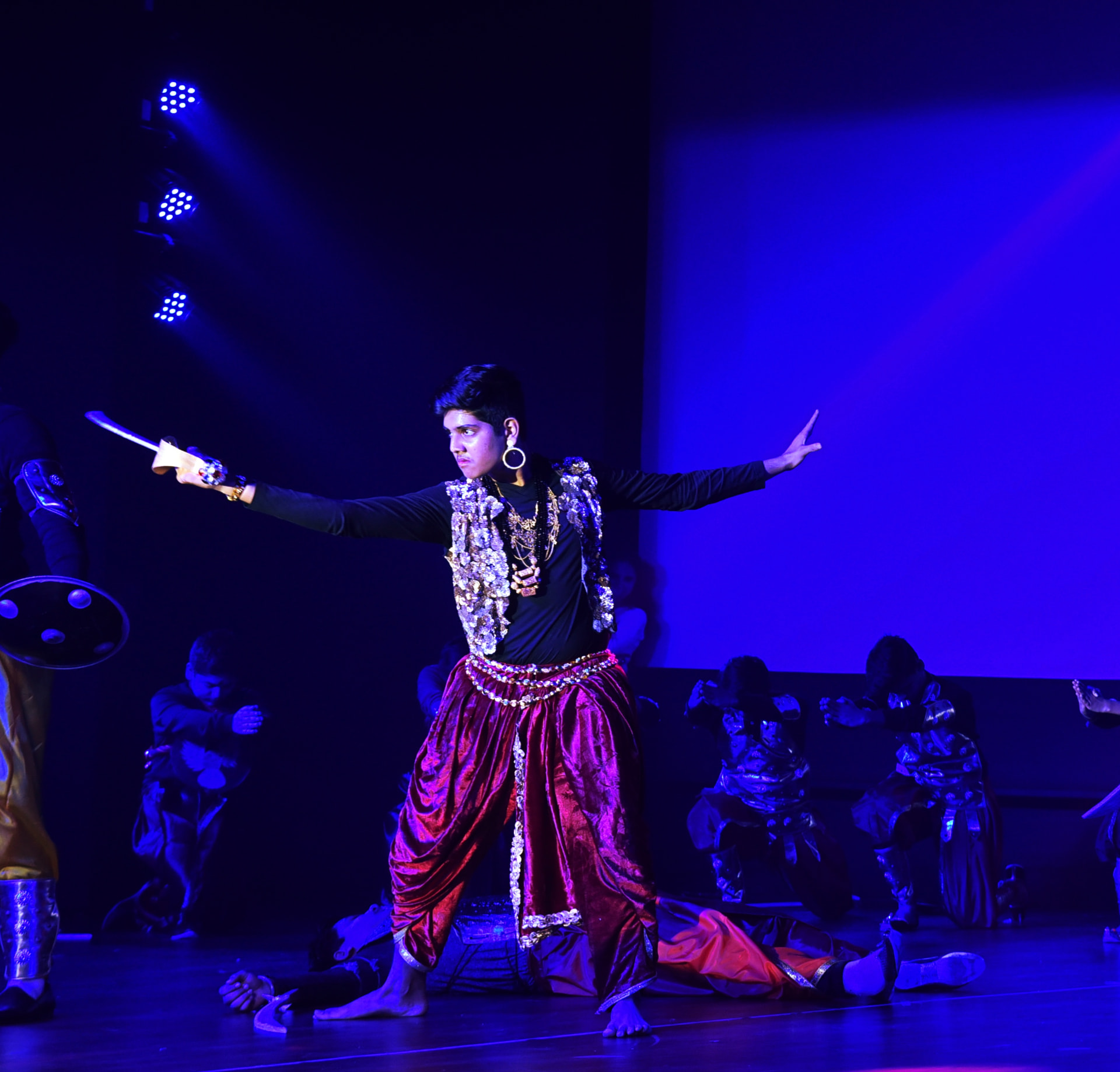 Student actor performing a warrior scene under blue stage lights